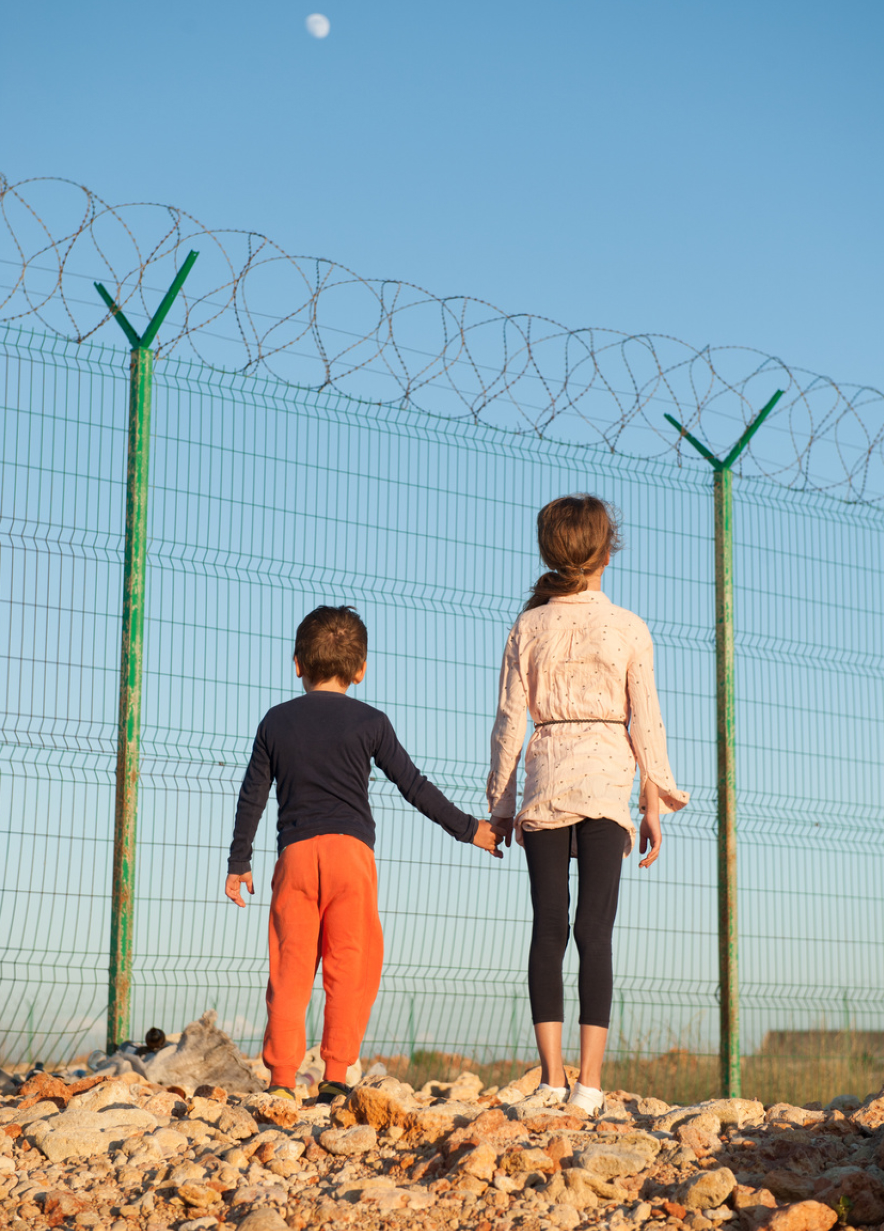 girl holding little boy's hand standing infront of barbwired fence